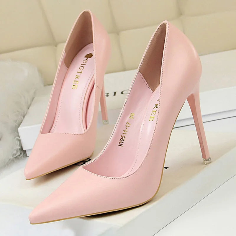 Elegant pink high heels with pointed toes and stiletto heels, displayed on a beige surface. The inner sole features a gold label print, with a soft backdrop enhancing the shoes.