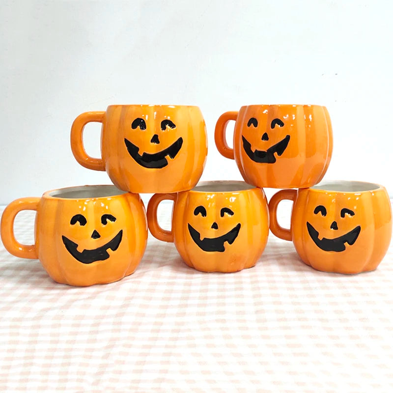 Five orange mugs with jack-o'-lantern faces are arranged in a pyramid on a checkered tablecloth. The mugs are bright with black smiley faces, ideal for Halloween.