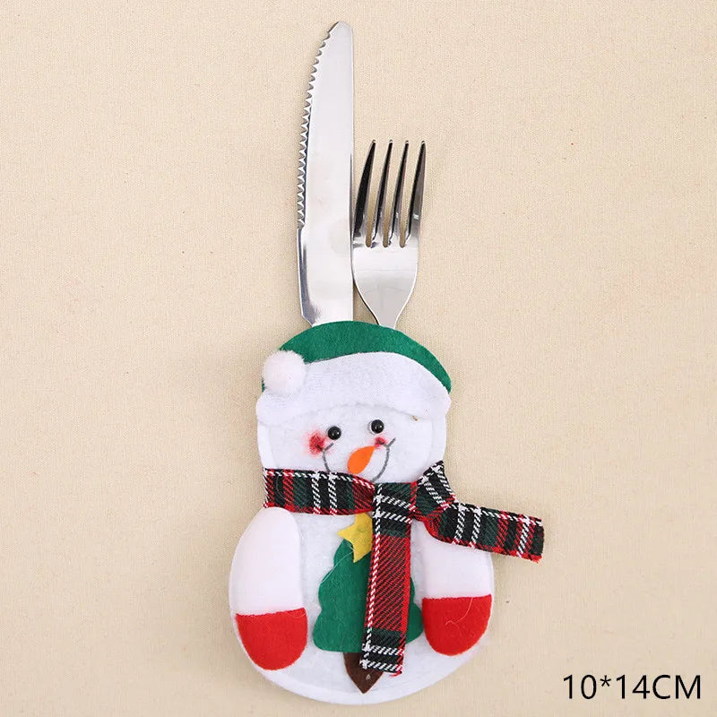 A snowman-themed cutlery holder featuring a fork and knife. The snowman has a green hat, plaid scarf, and red mittens. The dimensions are 10x14 cm.