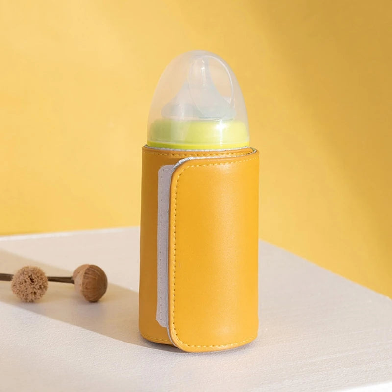Yellow insulated baby bottle holder on a white surface, with a transparent cap and green lid. Two dried flower heads lie beside it against a matching yellow background.