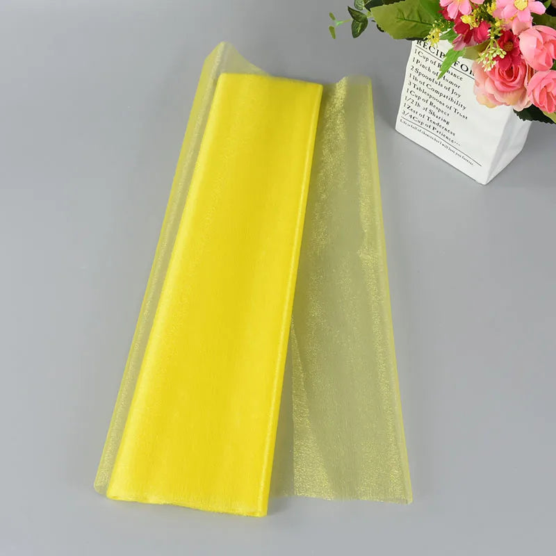 Yellow organza fabric laid on a gray surface next to a bouquet of pink flowers in white packaging.