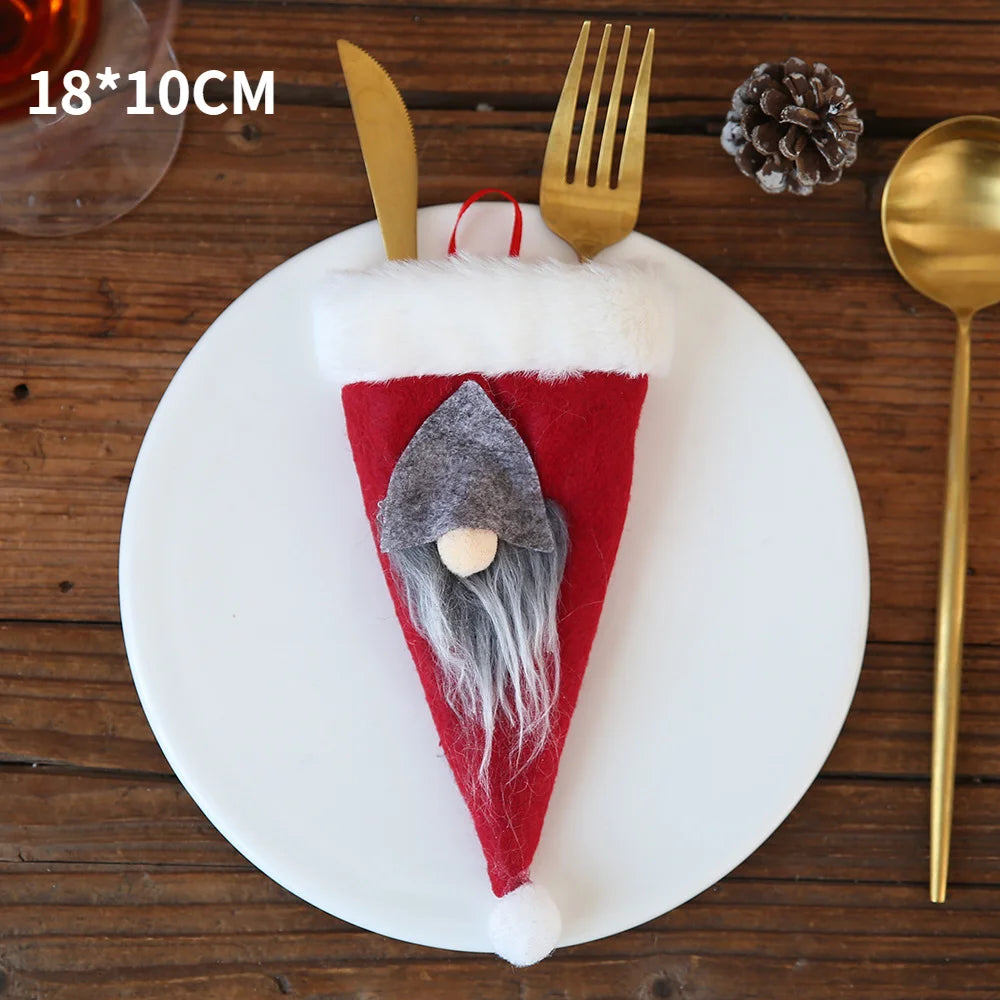 Festive utensil holder shaped like a gnome hat, featuring a red felt with white trim and gray beard, holding a gold fork and knife on a white plate with pinecone accent.