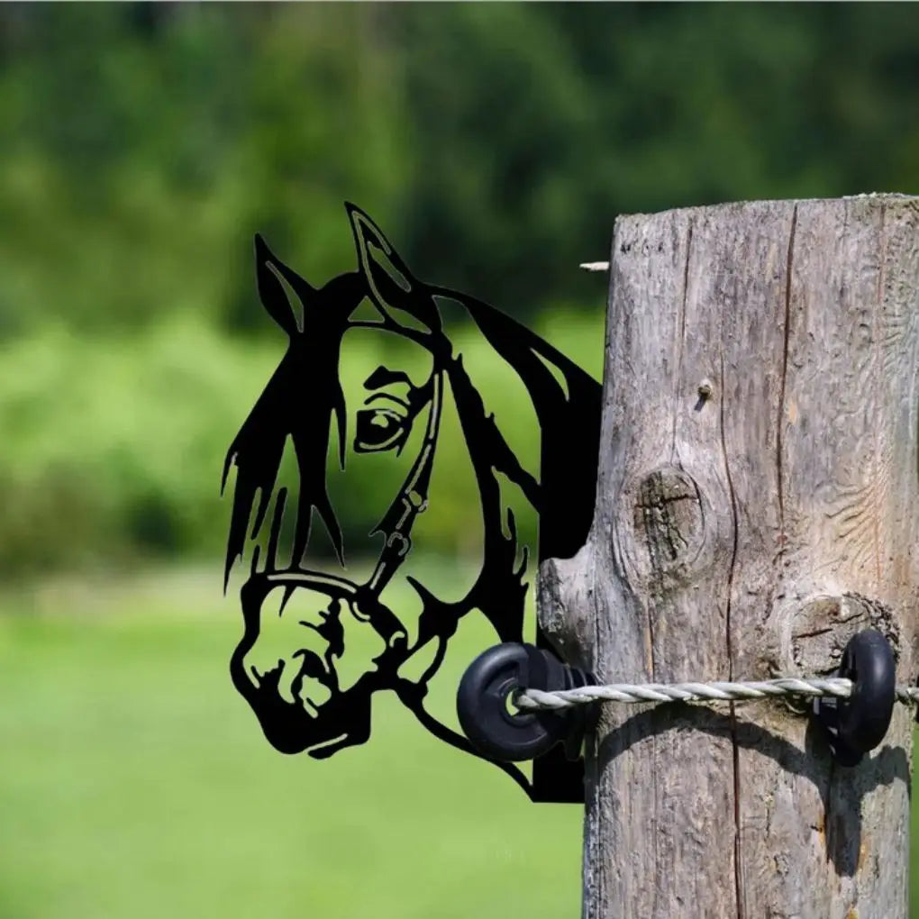 Silhouette of a horse's head attached to a wooden post with a black insulator and wire, set against a blurred green background of grass and trees.