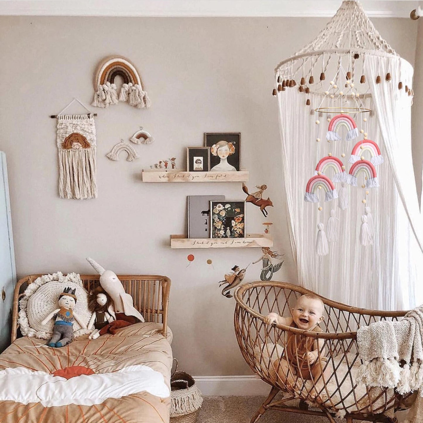 A cozy nursery with a wicker crib and smiling baby. Decor includes rainbow wall hangings, a canopy, stuffed toys on a bed, floating shelves, and whimsical prints on a neutral wall.