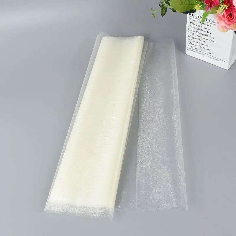 Folded ivory fabric placed on a light gray surface, beside a potted plant with pink flowers and a book with partially visible text.