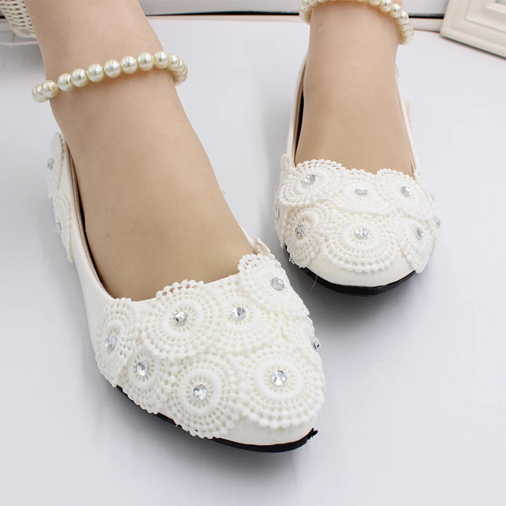 Elegant cream flats with intricate lace patterns and rhinestone embellishments. Paired with pearl anklets, the shoes exude a delicate and sophisticated charm.