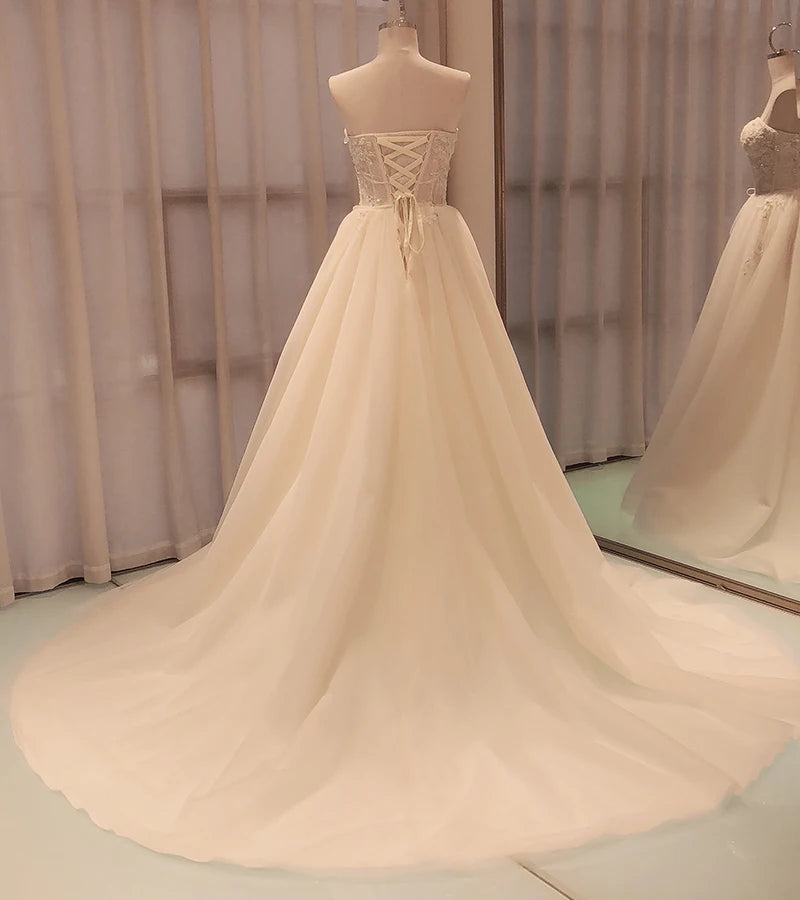 Elegant strapless wedding gown with a lace-up back and long flowing train on a mannequin, reflected in a mirror against soft, sheer curtains.