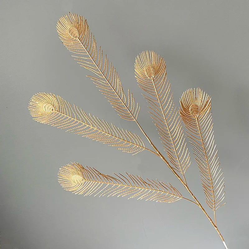 Golden peacock feathers with intricate detailing fan outward against a neutral gray background, creating an elegant and artistic visual.