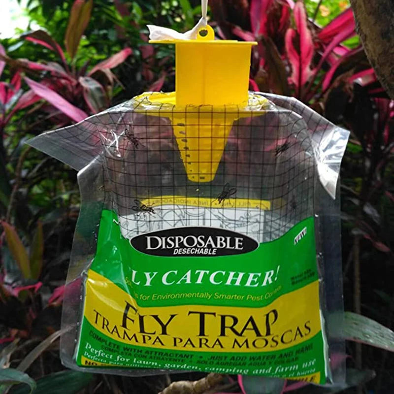 Disposable fly trap hanging outdoors among plants, with a yellow plastic top and a transparent bag showing flies inside. The bag is labeled in English and Spanish.