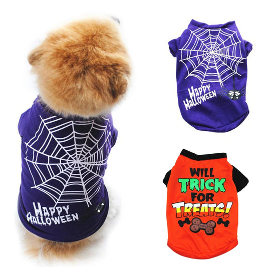 Dog in a purple “Happy Halloween” shirt with a spider web design. Nearby are two shirts: one identical purple with web and a red one saying “Will Trick for Treats” with bone graphics.