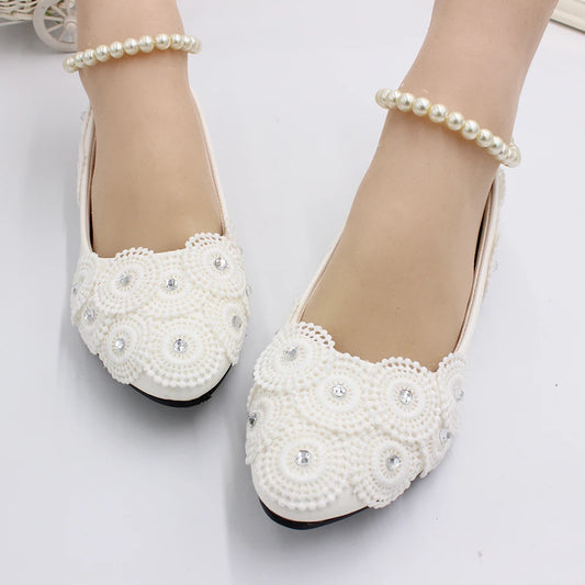 White flat shoes adorned with intricate beadwork and rhinestones, paired with delicate pearl anklets on a white background.