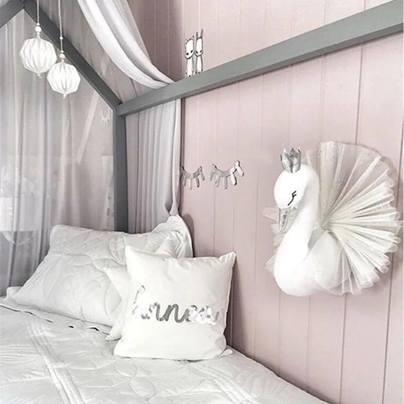 Cozy bedroom with a bed featuring white linens and a personalized pillow. A swan wall decoration with a crown and fans adds charm. Soft lighting and curtains create a serene atmosphere.