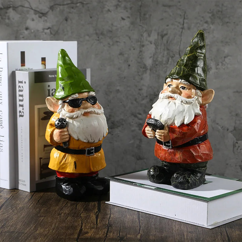 Two garden gnomes with beards and green hats are on display. One wears sunglasses and holds a hose, dressed in yellow. The other in red holds a lantern, standing on a book.
