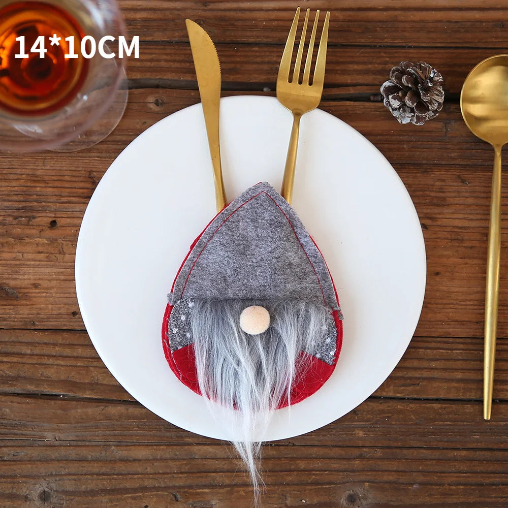 Gold utensils in a felt gnome holder with a long beard, placed on a white plate over a wooden table. A small pinecone decorates the setting. Dimensions noted as 14x10 cm.