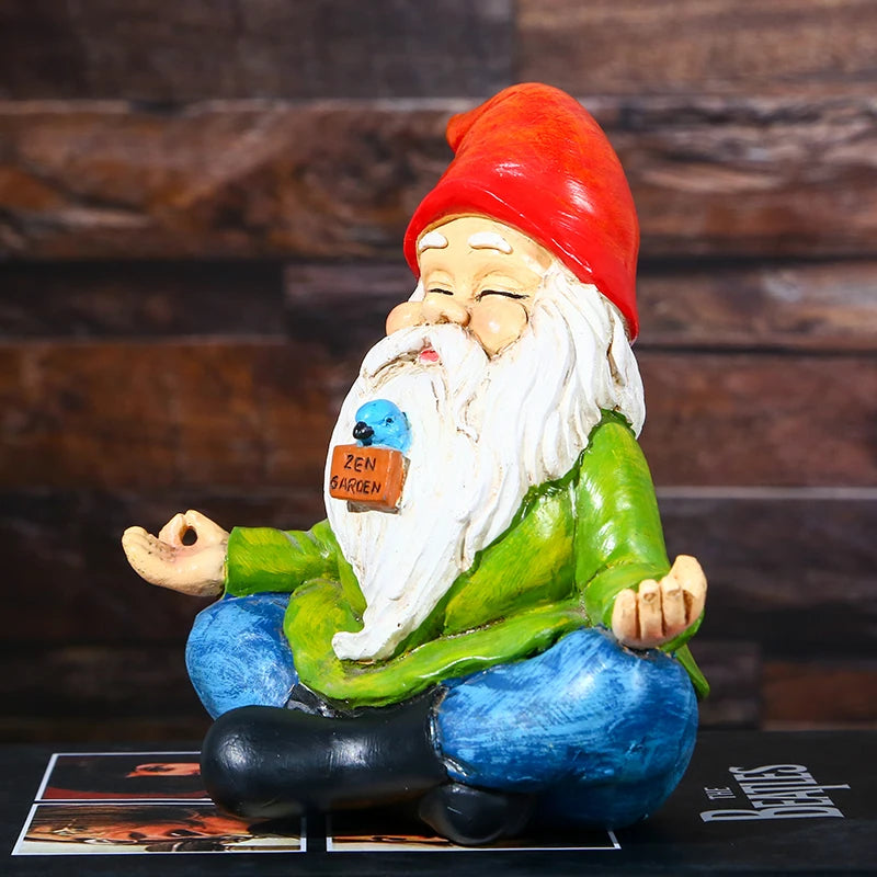 A meditating garden gnome wearing a red hat and green coat sits cross-legged. It has a sign labeled "Zen Garden" and features a small blue bird on its beard.