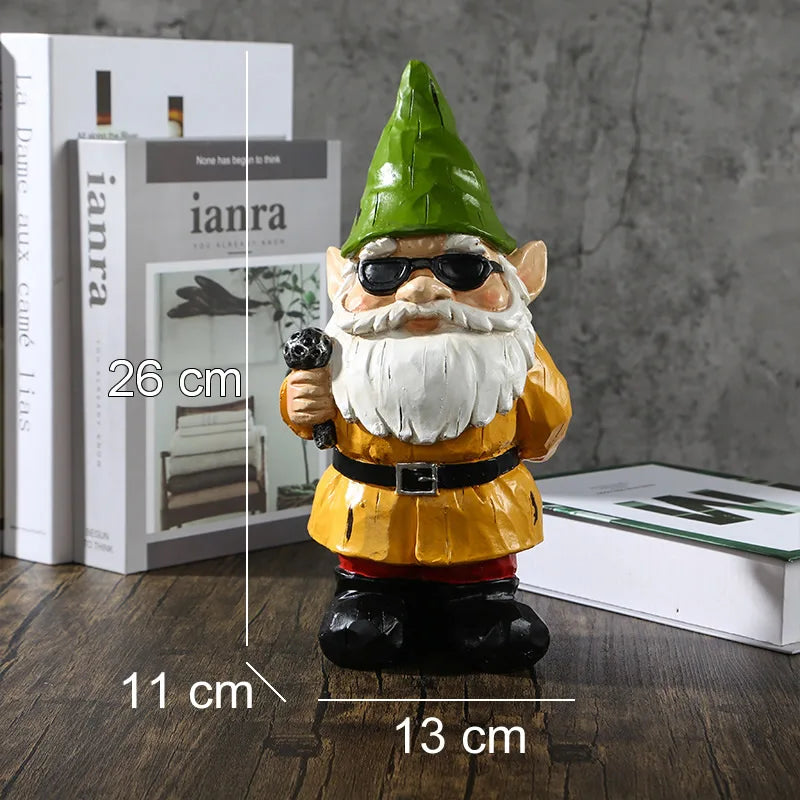 Garden gnome statue with a green hat and sunglasses, holding a microphone. It measures 26 cm tall, 13 cm wide, and 11 cm deep. Books in the background on a wooden surface.