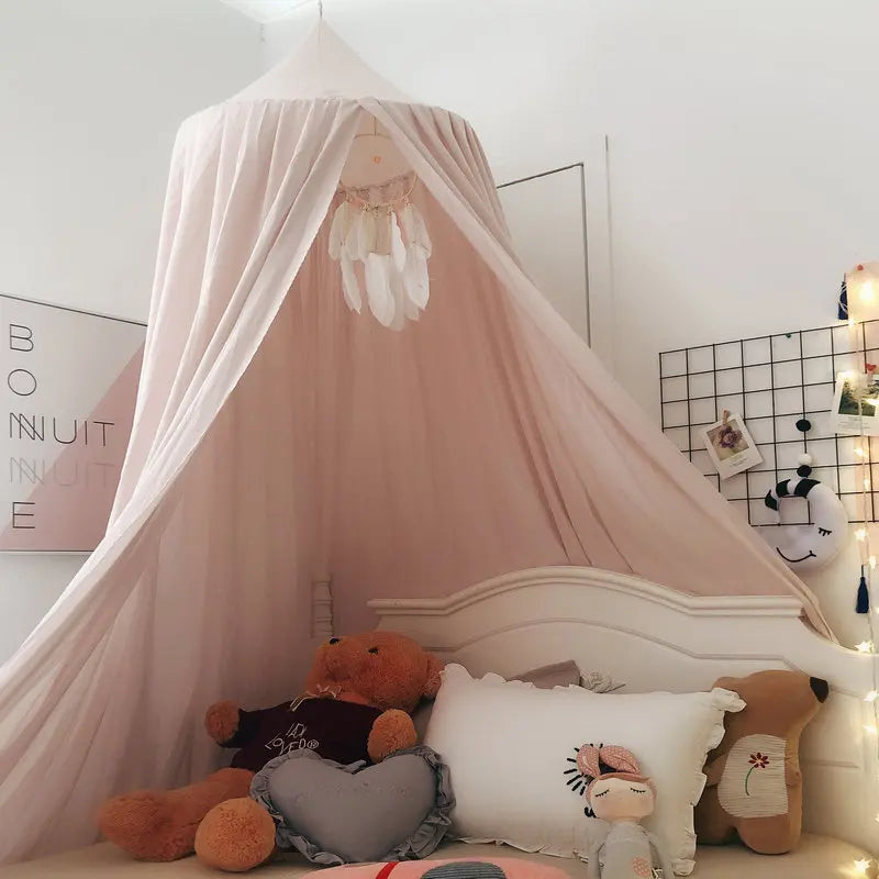 Cozy children's bedroom with a canopy over a bed adorned with cushions and plush toys. A dreamcatcher hangs inside the canopy. Soft lighting and decorative items complete the decor.