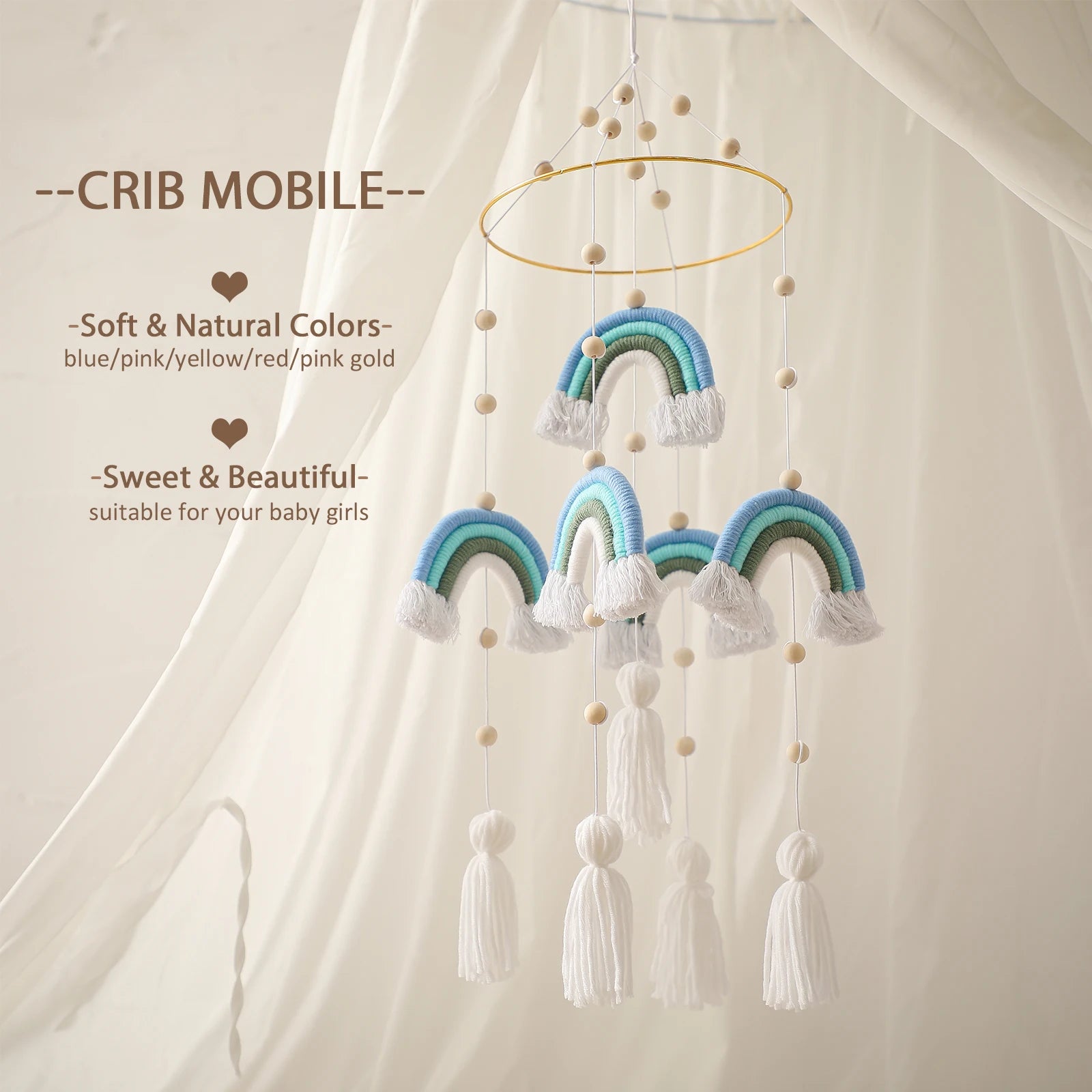 A rainbow crib mobile with soft colors, featuring blue and green rainbows, white tassels, and wooden beads. It hangs from a circular frame against a cream curtain backdrop.