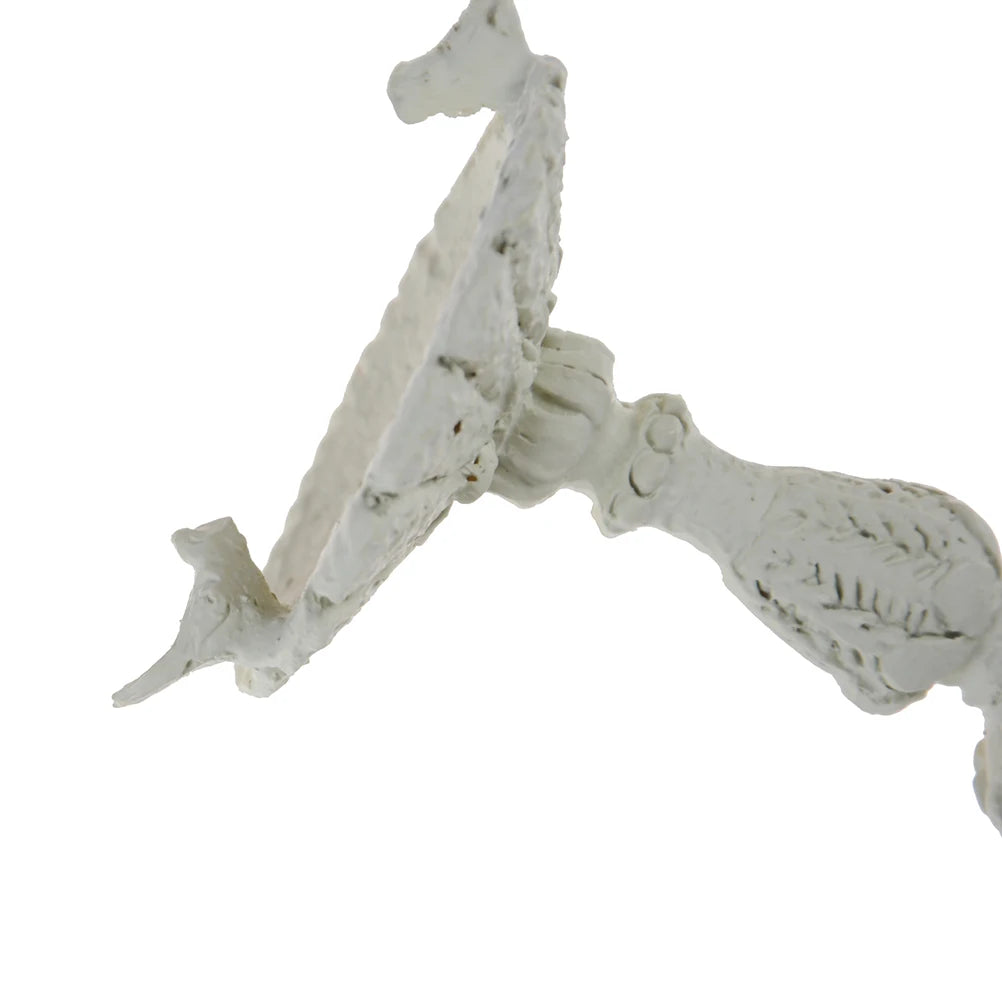 Close-up view of an ornately carved, white decorative object with leafy patterns. The focus is on a curved section with floral details, set against a plain background.