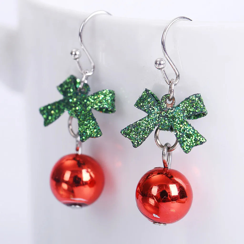 Green glitter bow earrings with dangling red baubles on silver hooks, reminiscent of holiday ornaments, resting against a white background.