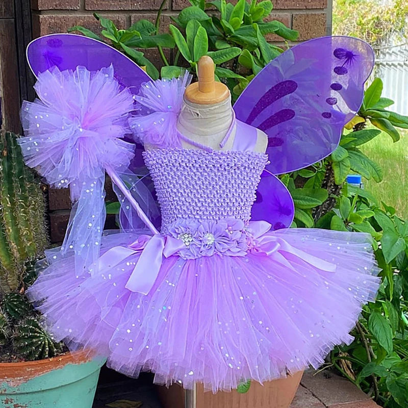 Purple fairy dress with tulle skirt and floral belt, adorned with matching wings and a wand, displayed outdoors near a cactus and lush green plants.