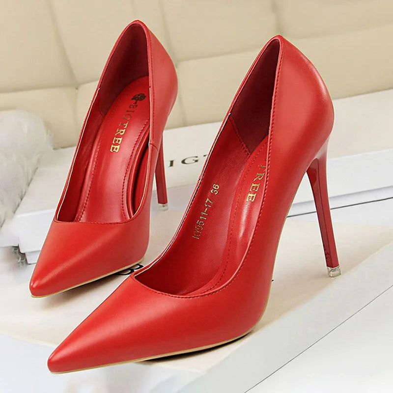 A pair of sleek, red high-heeled pumps with pointed toes on a light-colored surface. The shoes have an elegant design, suitable for formal or stylish occasions.