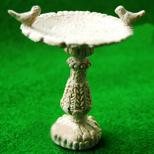 A decorative stone birdbath with intricate carvings, featuring two small birds perched on the edge. The background is a vibrant green, simulating grass.