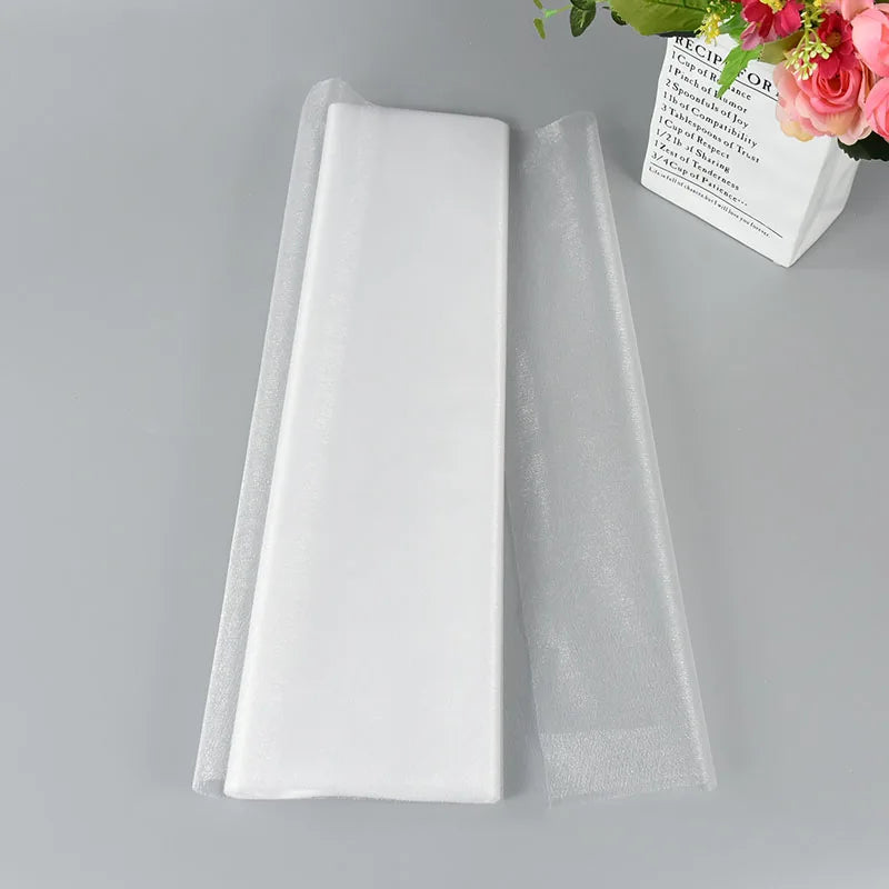 A folded white sheet of fabric on a gray surface, with a bouquet of pink and red flowers in a vase nearby.