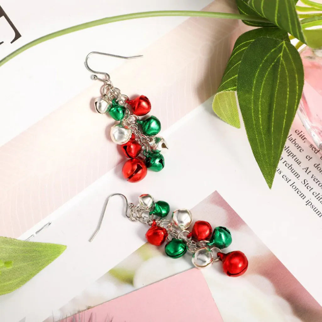 Festive earrings with red, green, and silver jingle bells on a silver chain, displayed on a floral background with green leaves.