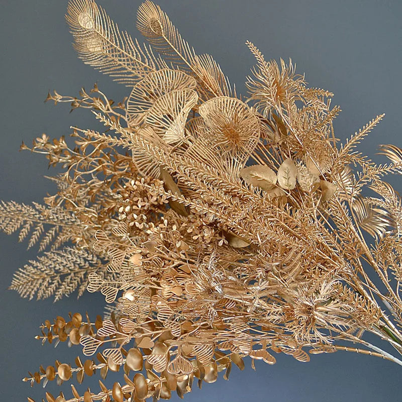 A bouquet of intricately arranged metallic gold foliage and ferns against a gray background, showcasing detailed textures and a variety of leaf shapes.