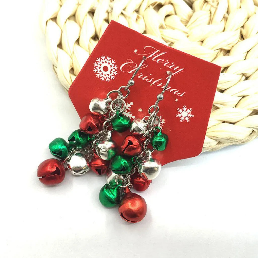 Dangling Christmas earrings with red, green, and silver bells, displayed on a red card with "Merry Christmas" inscribed, on a woven background.