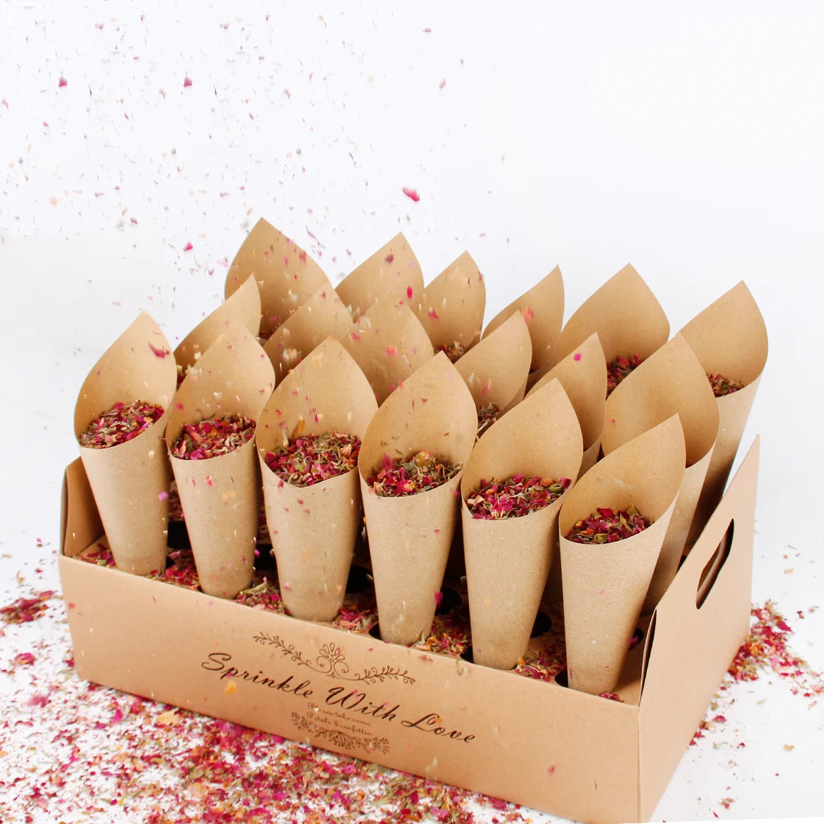 A box filled with brown paper cones containing colorful dried flower petals labeled "Sprinkle With Love." Petals are scattered around, creating a festive atmosphere.