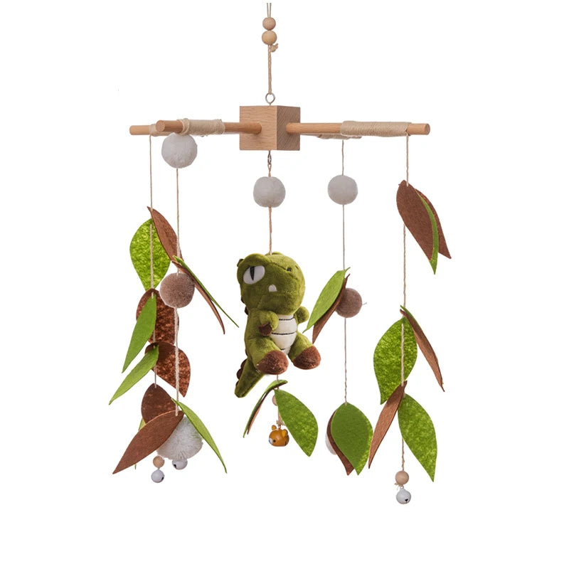 Hanging baby mobile with a green dinosaur centerpiece surrounded by felt leaves and wooden beads on strings, providing a whimsical, natural theme.