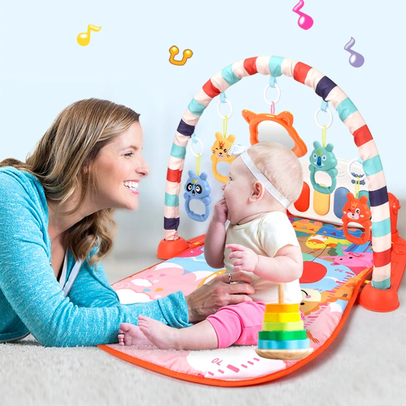 A woman and baby play on a colorful activity mat with hanging toys. The baby, wearing a headband, faces the woman, surrounded by musical notes floating in the air.