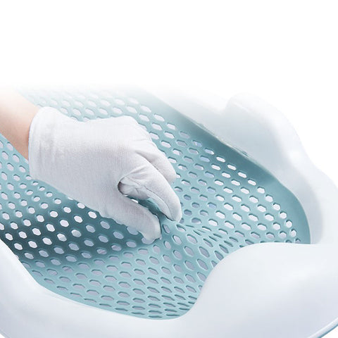 A hand wearing a white glove is pressing into a light blue, perforated, flexible surface, surrounded by a white plastic frame. The surface appears soft and cushioned.