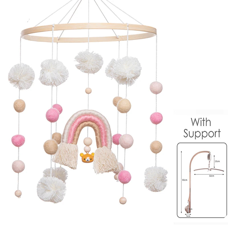 Baby mobile with pink and beige felt balls and pom-poms, featuring a rainbow and bear charm. Includes a diagram of support stand with measurements.