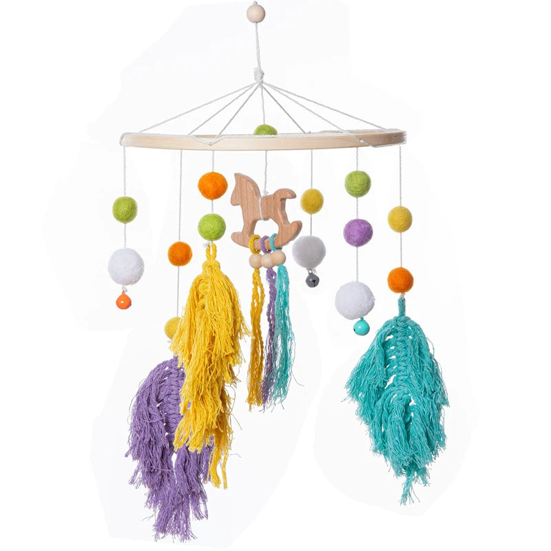 Colorful baby mobile with felt balls in orange, green, purple, and white. Features teal, yellow, and purple tassels, with a central wooden horse figure.