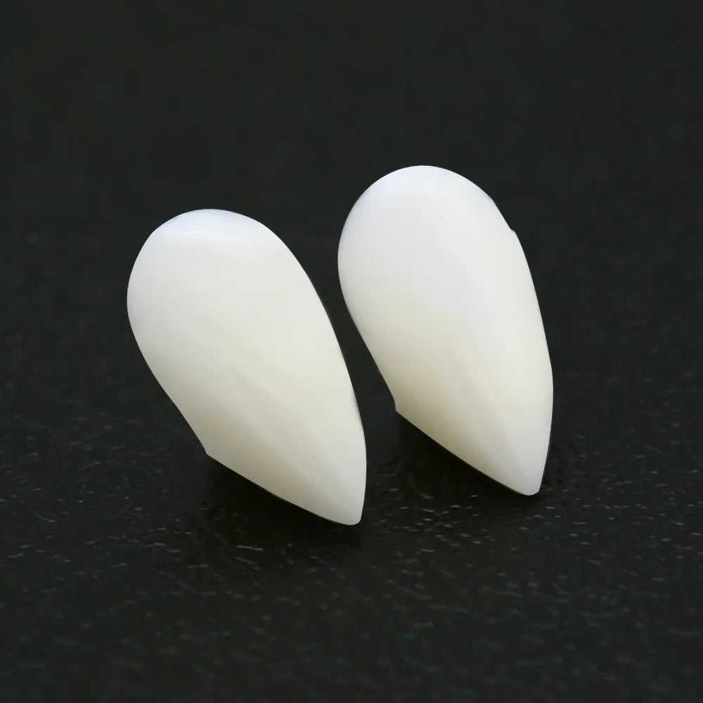 Two white, pointed ear prosthetics on a dark surface, resembling natural ears with a sleek, smooth design.