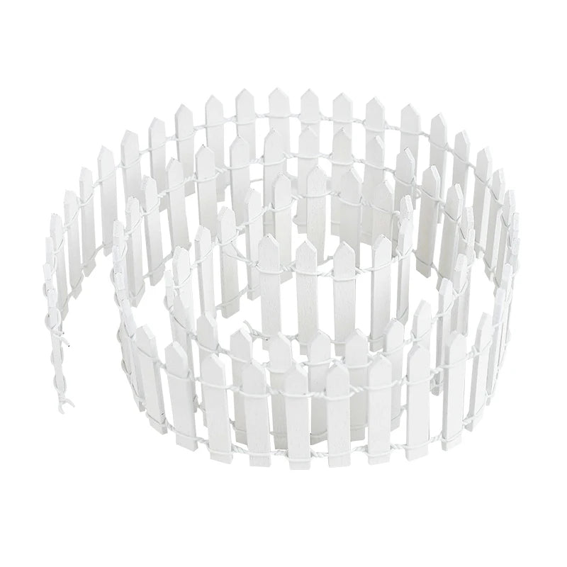 A coiled miniature white picket fence, made of small, evenly spaced vertical slats connected by wires, against a plain white background.