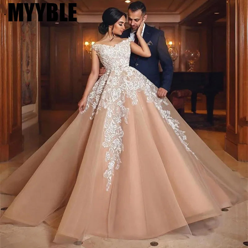 A woman in an elegant blush wedding gown with intricate white lace stands with a man in a suit in a luxurious wood-paneled room, exuding a romantic and sophisticated ambiance.