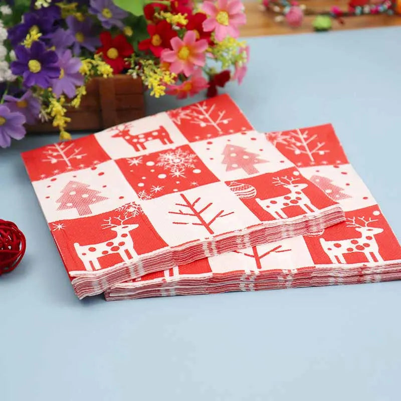 Festive red and white napkins with reindeer, snowflakes, and tree patterns are stacked on a blue surface. Colorful flowers are in the background for added decoration.