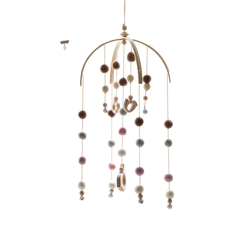 Hanging mobile with wooden arcs, colorful felt pom-poms, and wooden beads, creating a whimsical design. It's suspended by a string and small wooden ring hanger.