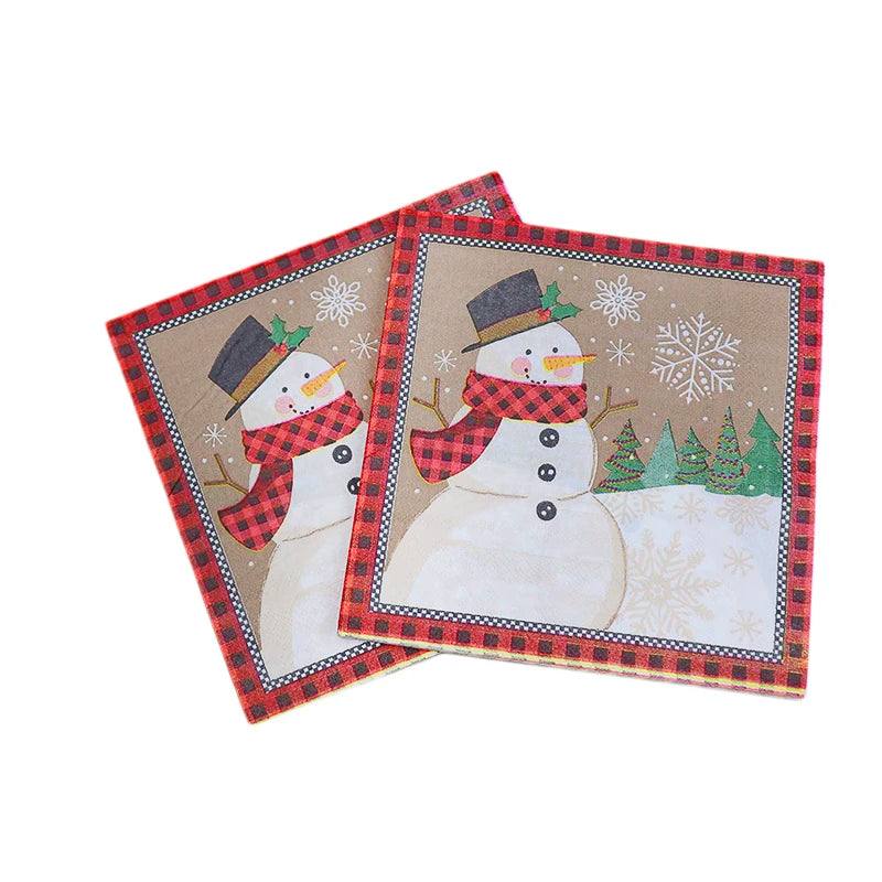 Two festive napkins featuring a snowman wearing a black hat and red scarf, surrounded by snowflakes and trees. The border is a red and black plaid pattern.