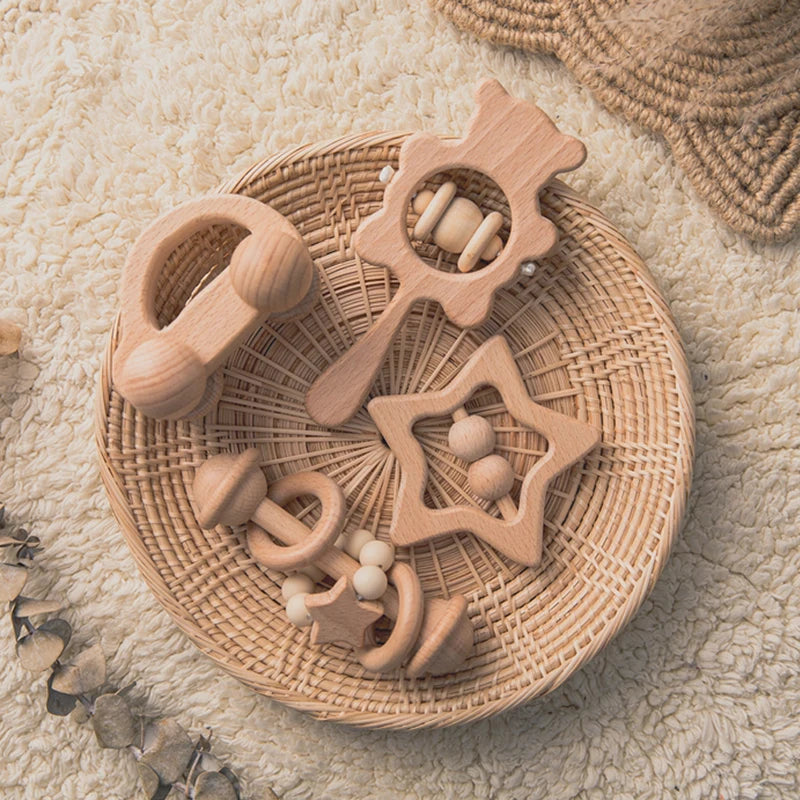 A round woven basket holds various wooden baby rattles and teethers on a fluffy cream carpet. The toys are in natural wood tones, shaped like stars and abstract forms.
