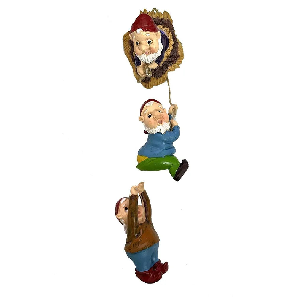 Three playful gnome figurines are depicted vertically. The top gnome peeks out of a tree hollow, holding a rope from which the other two gnomes hang, creating a whimsical scene.