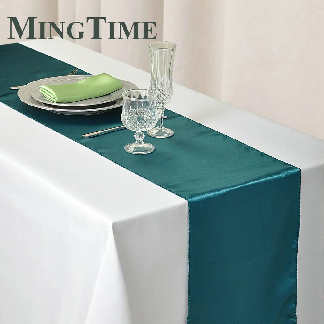 Elegant dining table with a white cloth and teal runner, set with white plates, a green napkin, crystal glasses, and silverware. Text "MingTime" visible in the corner.