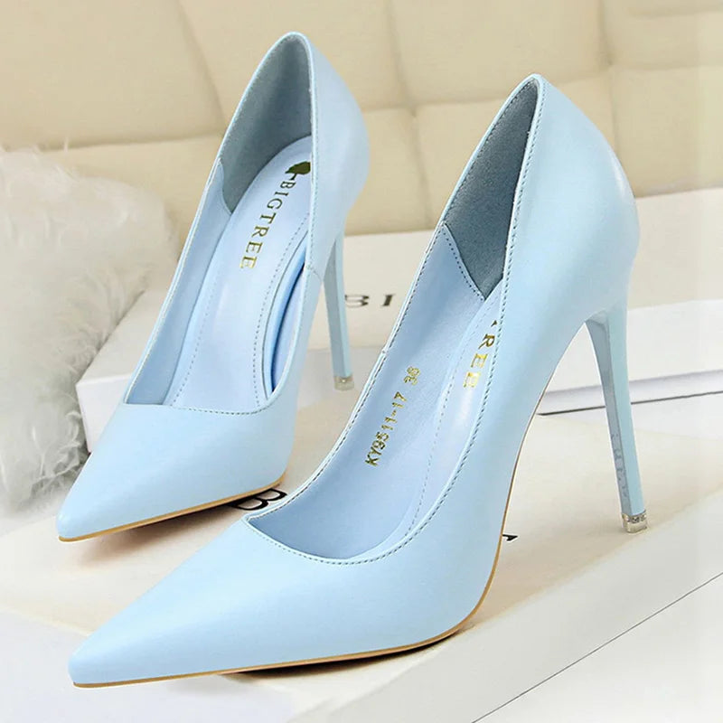 Light blue high-heeled shoes with a pointed toe design, placed on a white surface. The interior is lined with gold text. Background features a soft, blurred texture.