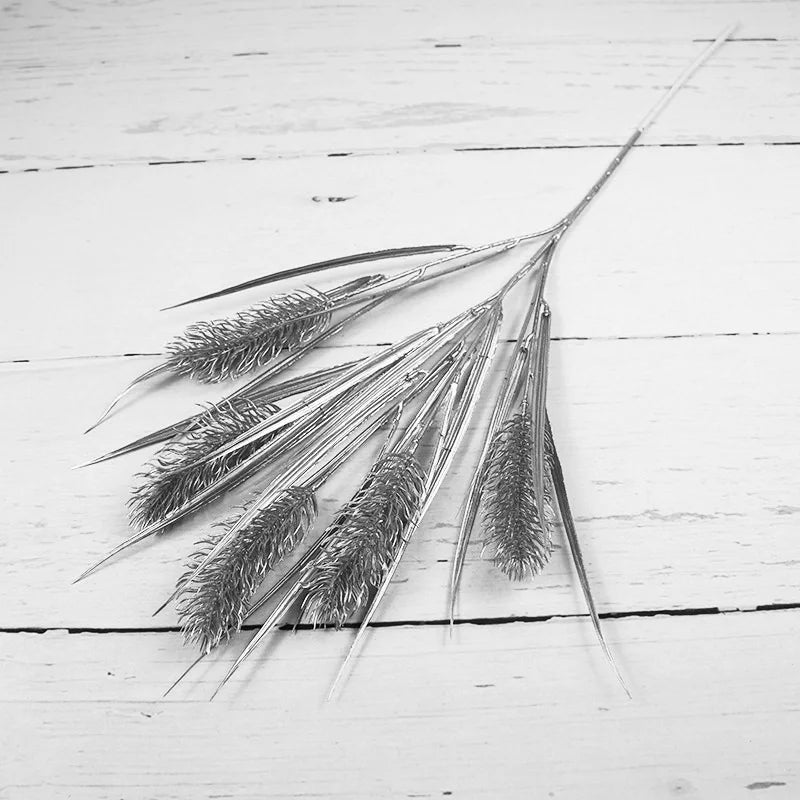 A black and white image of a bundle of textured wheat stems placed on a wooden surface. The stems fan outwards, showcasing intricate details and fine strands.