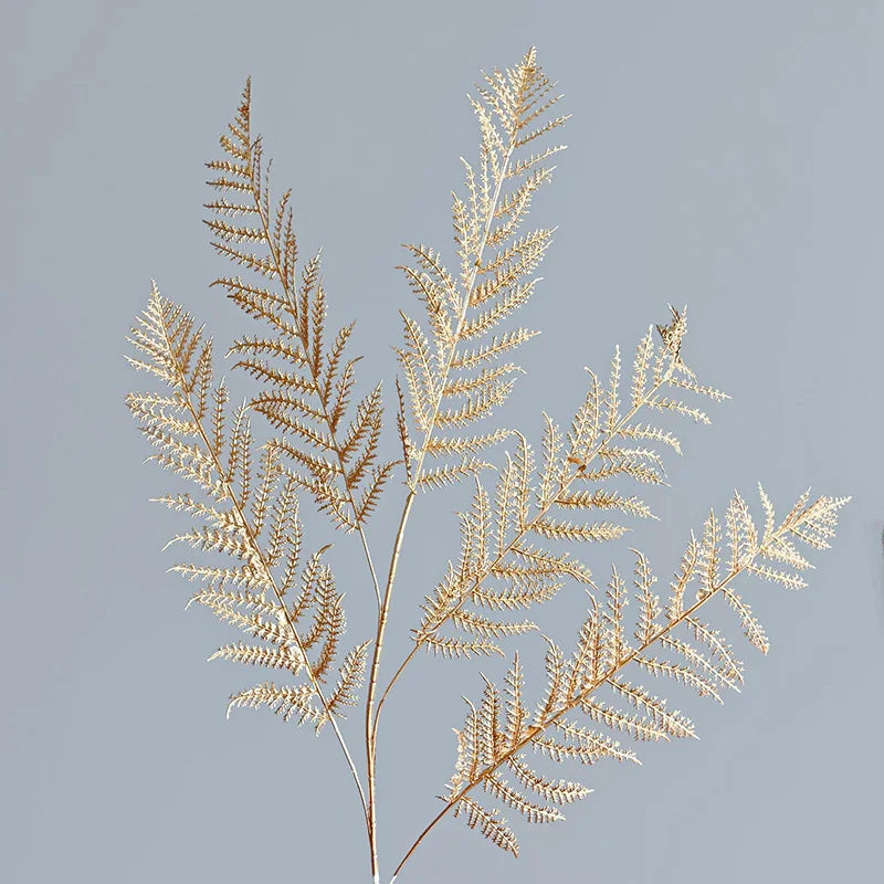 Delicate golden fern-like branches against a soft gray background, displaying intricate leaf patterns and a sense of natural elegance.