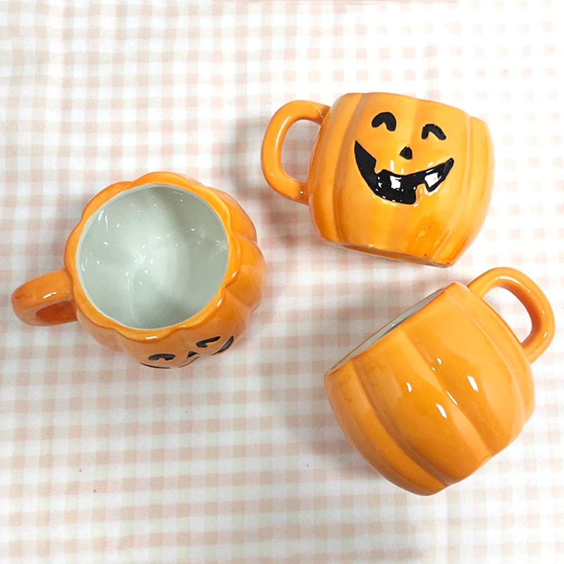 Three orange pumpkin-shaped mugs with smiling faces, one facing up and two sideways, on a light checkered cloth.